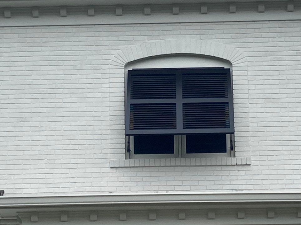 Bahama Shutters Lexington, KY A white brick building with a window with black shutters on it.