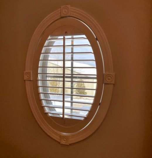 Oval Windows Lexington, KY An oval window with shutters on it and a view of a house