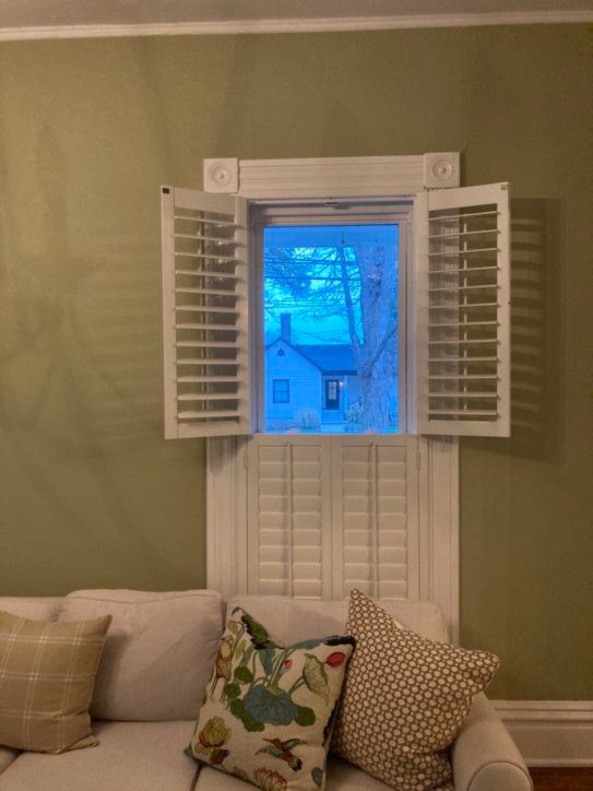 A living room with a couch and a window with shutters open