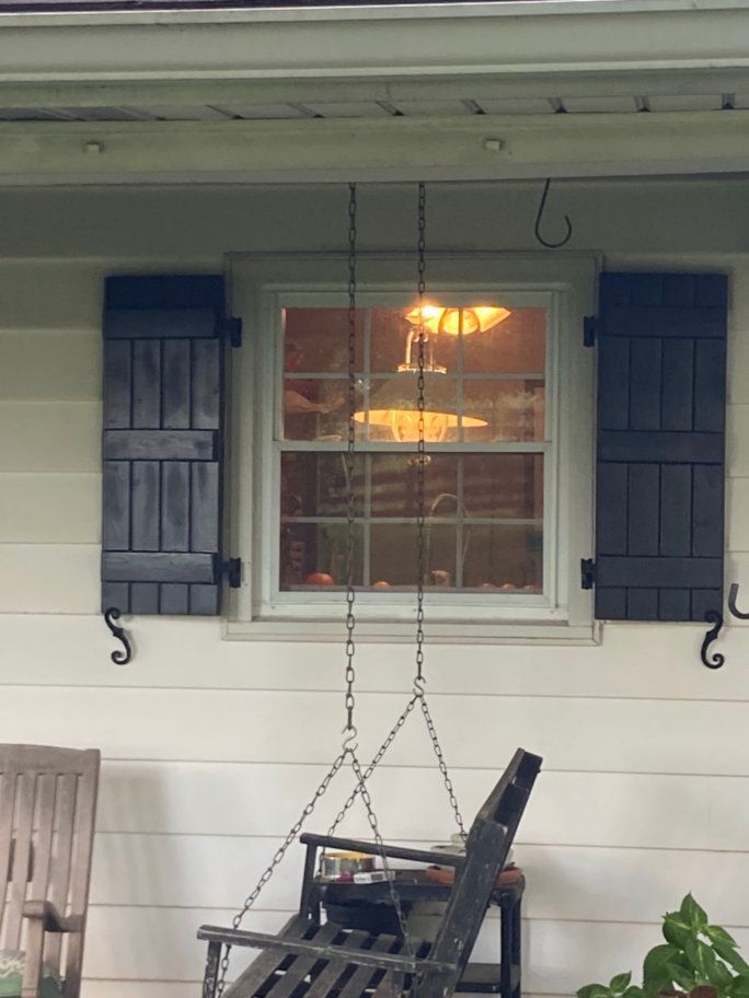 A porch with a swing and a window with black shutters