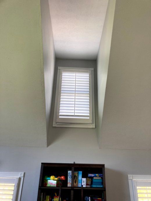 A room with a bookshelf and a window with shutters on it.