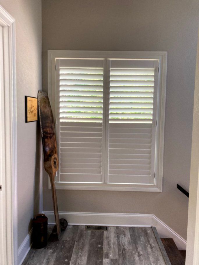 A room with a staircase and a window with shutters on it.
