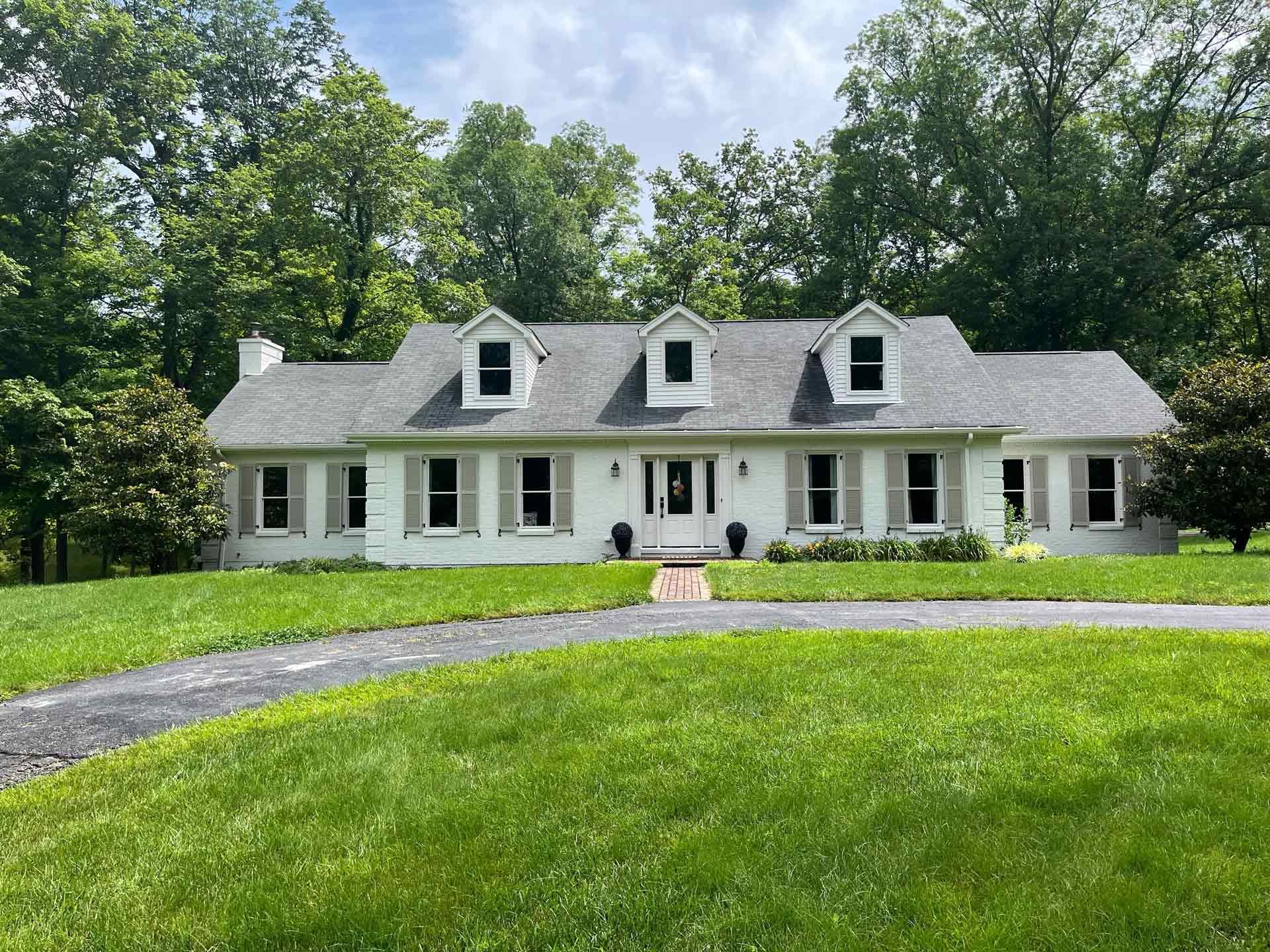 A large white house with a gray roof is sitting on top of a lush green field.