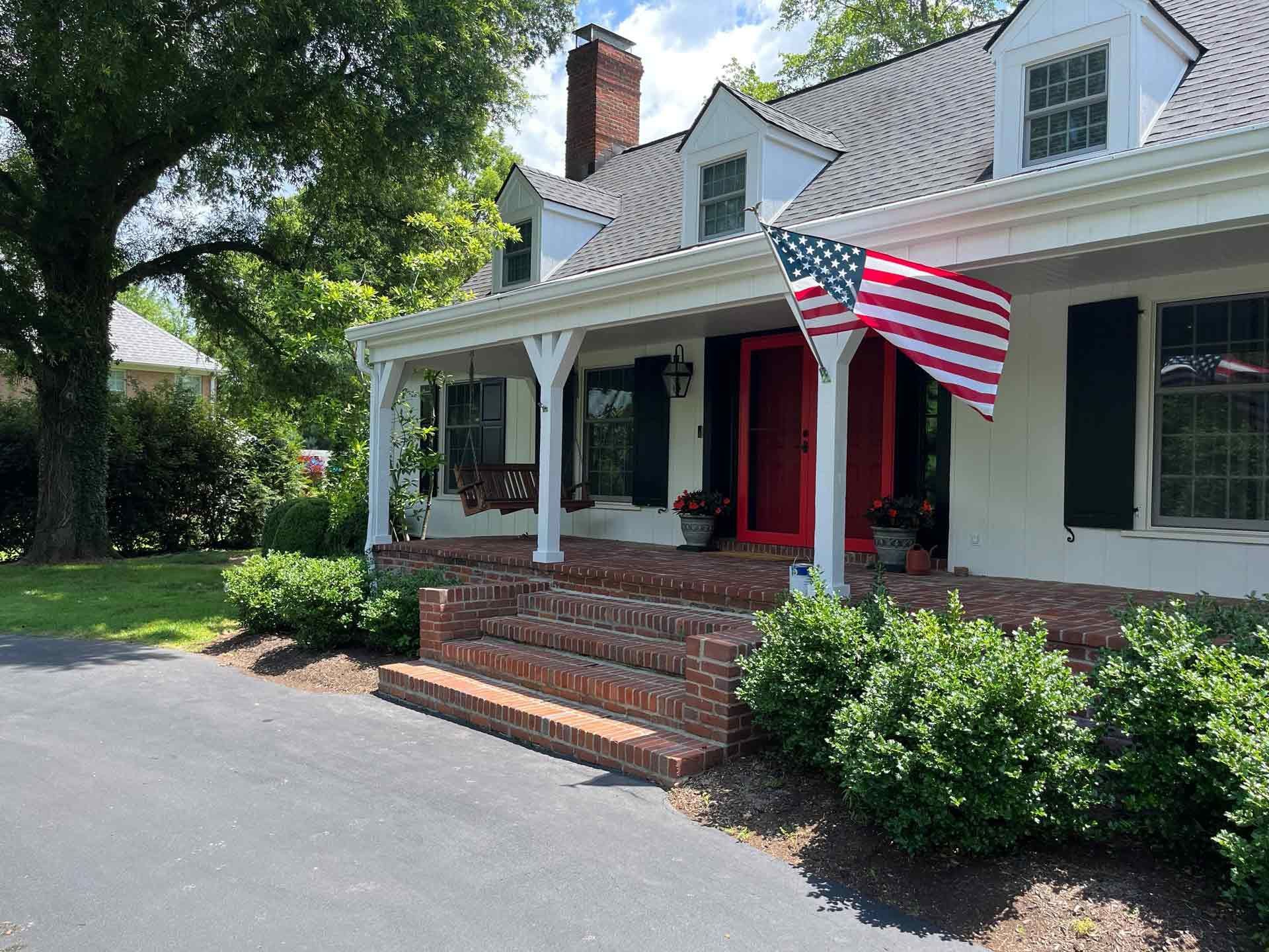 A white house with a red door and an american flag on the porch.