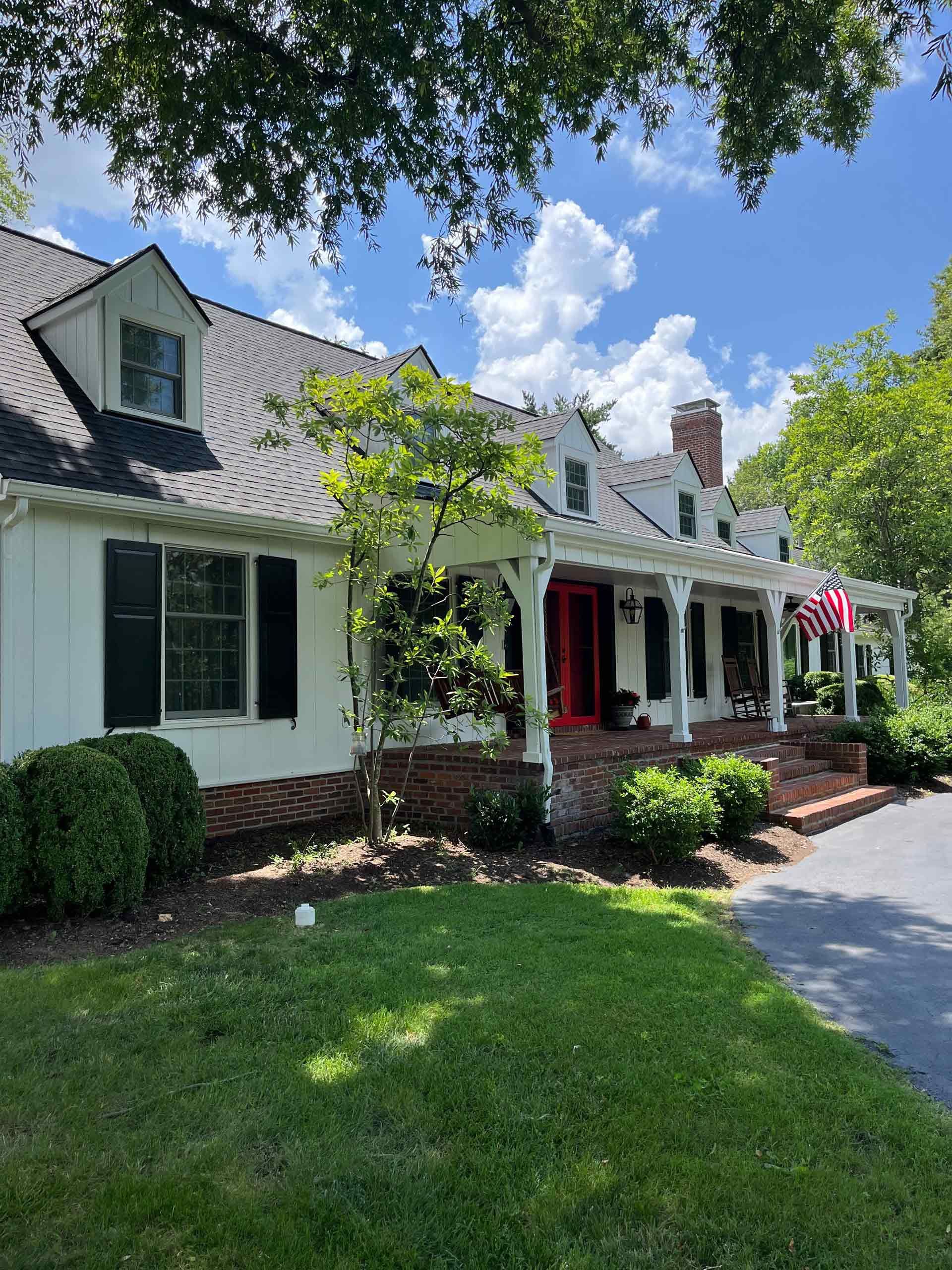 A white house with black shutters and a red door is sitting on top of a lush green lawn.