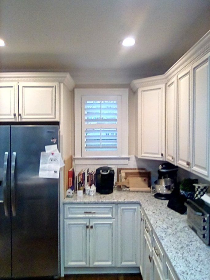A kitchen with white cabinets , stainless steel appliances , granite counter tops and a refrigerator.