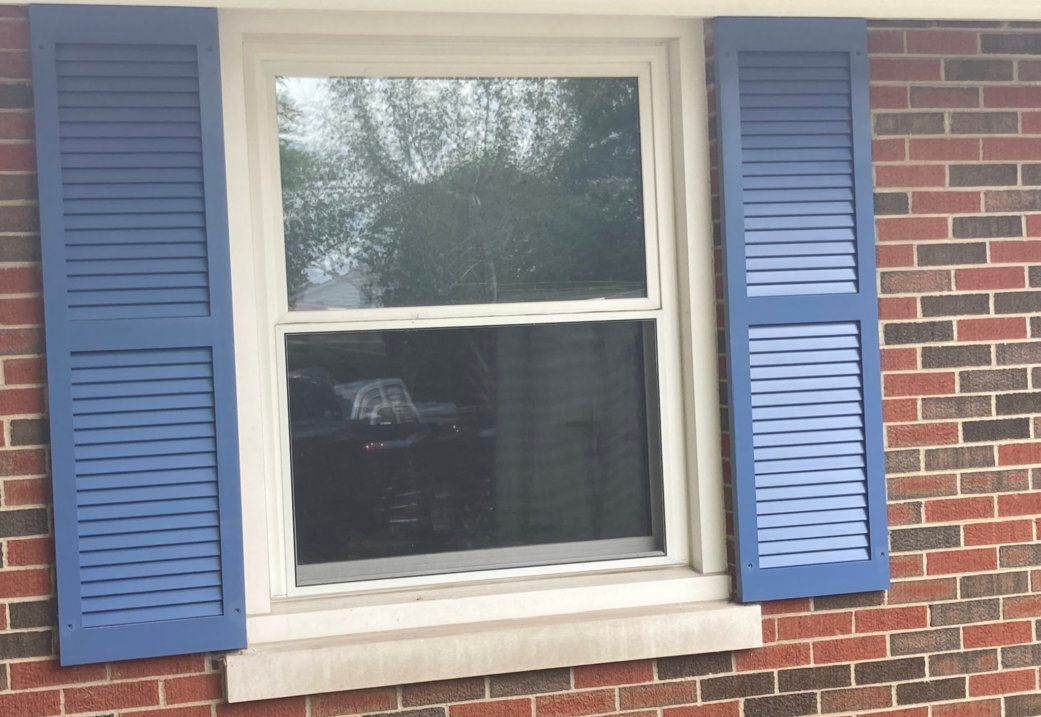 Louvered Shutters Lexington, KY A window with blue shutters on a brick wall.