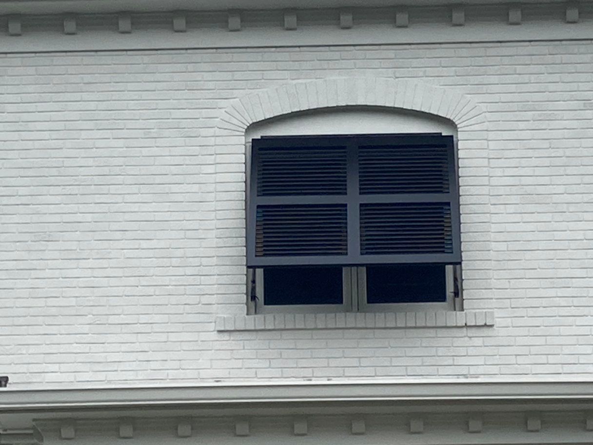 A white brick building with a window with black shutters