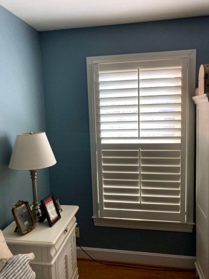 A bedroom with blue walls and white shutters on the window.