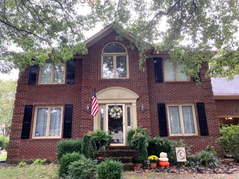 A large brick house with black shutters and a flag in front of it.