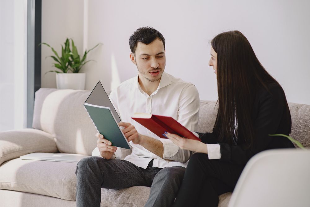 Man and woman reviewing documents, seated on a couch in an office setting, focused.