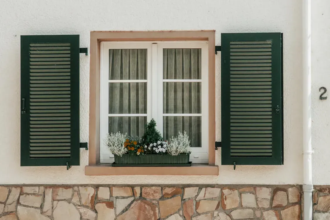 A window with green shutters and a flower box on it.