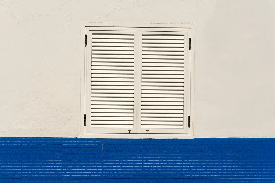 A white window with shutters on a blue and white wall.