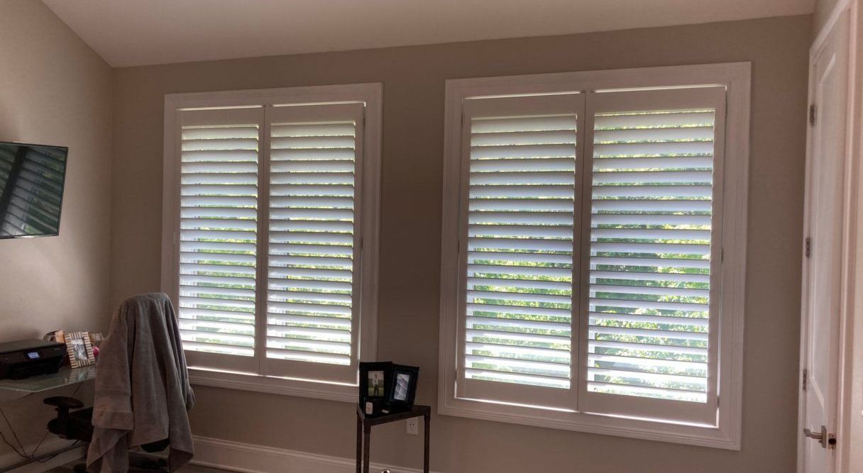 A bedroom with two windows and white shutters on them.