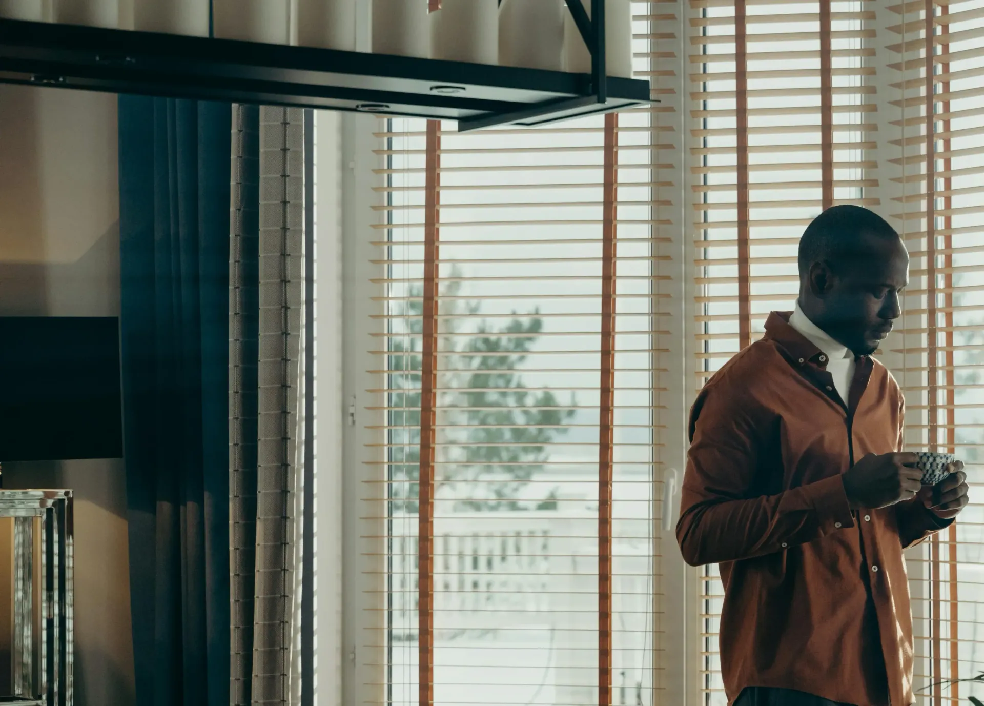 A man is standing in front of a window holding a cup of coffee.