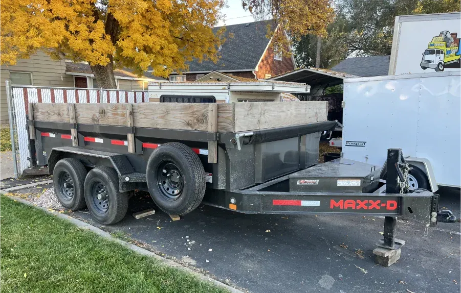 A dump trailer is parked in a driveway next to a white trailer.