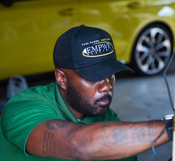 Man in green shirt and black cap working beside a yellow car in a garage