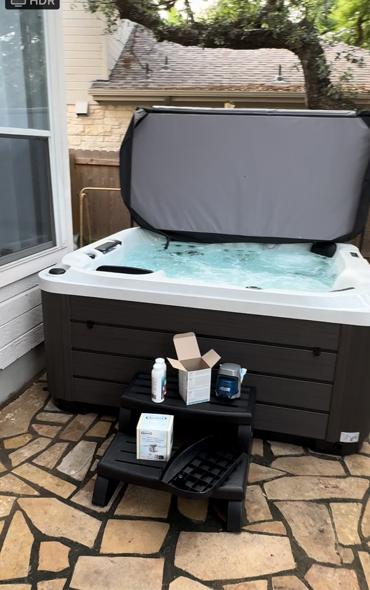 A hot tub is sitting on a stone patio with the lid open.