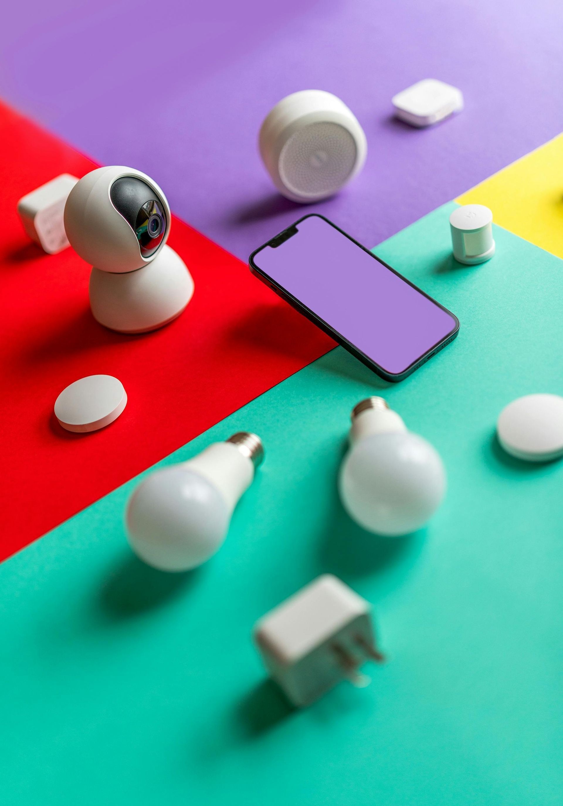 A smart phone is surrounded by light bulbs and a camera on a colorful surface.