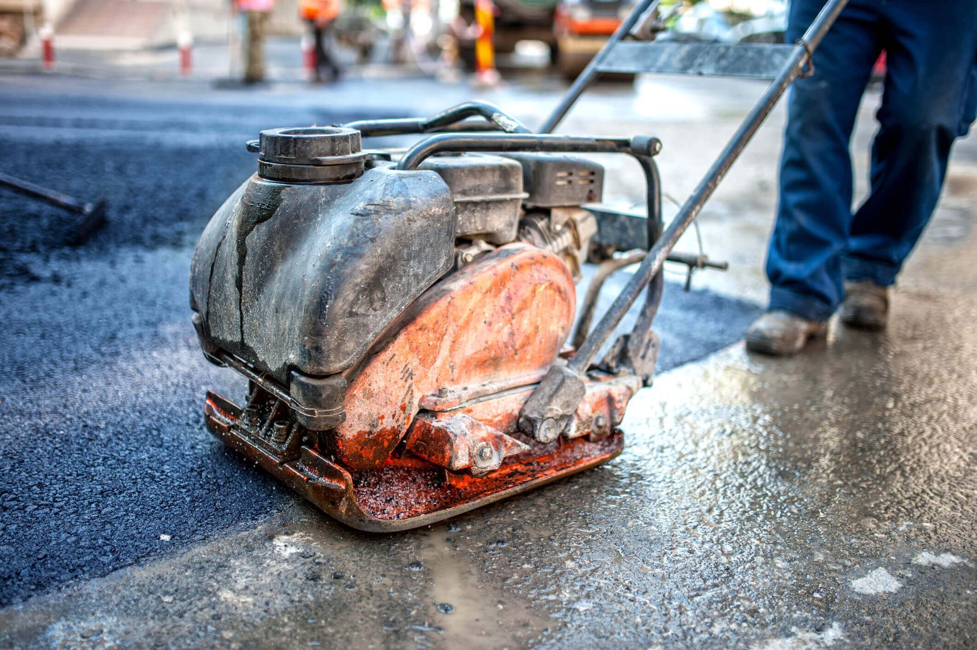 A man is using a compactor to compact asphalt on a road.
