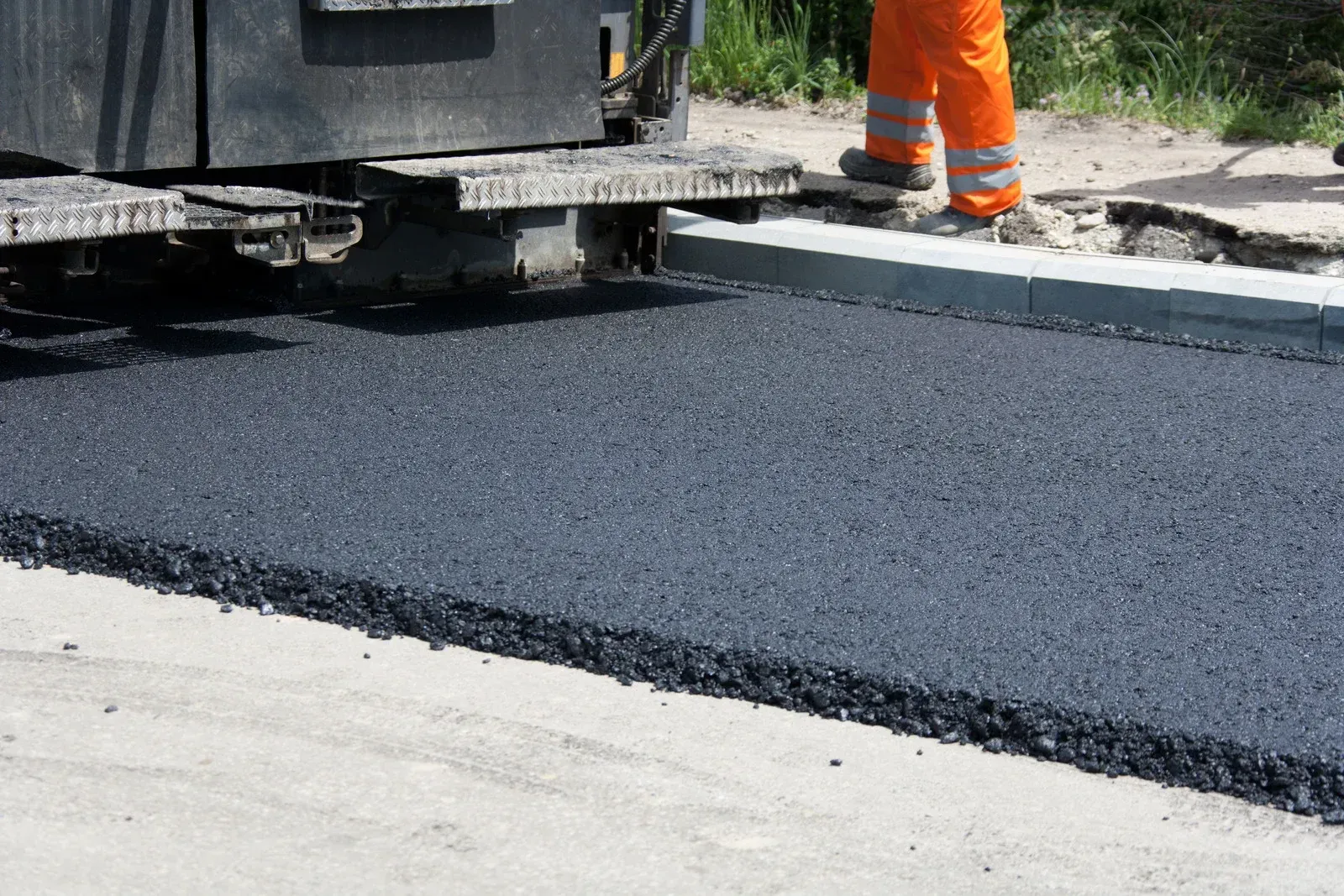 A man is standing next to a machine that is laying asphalt on a road.