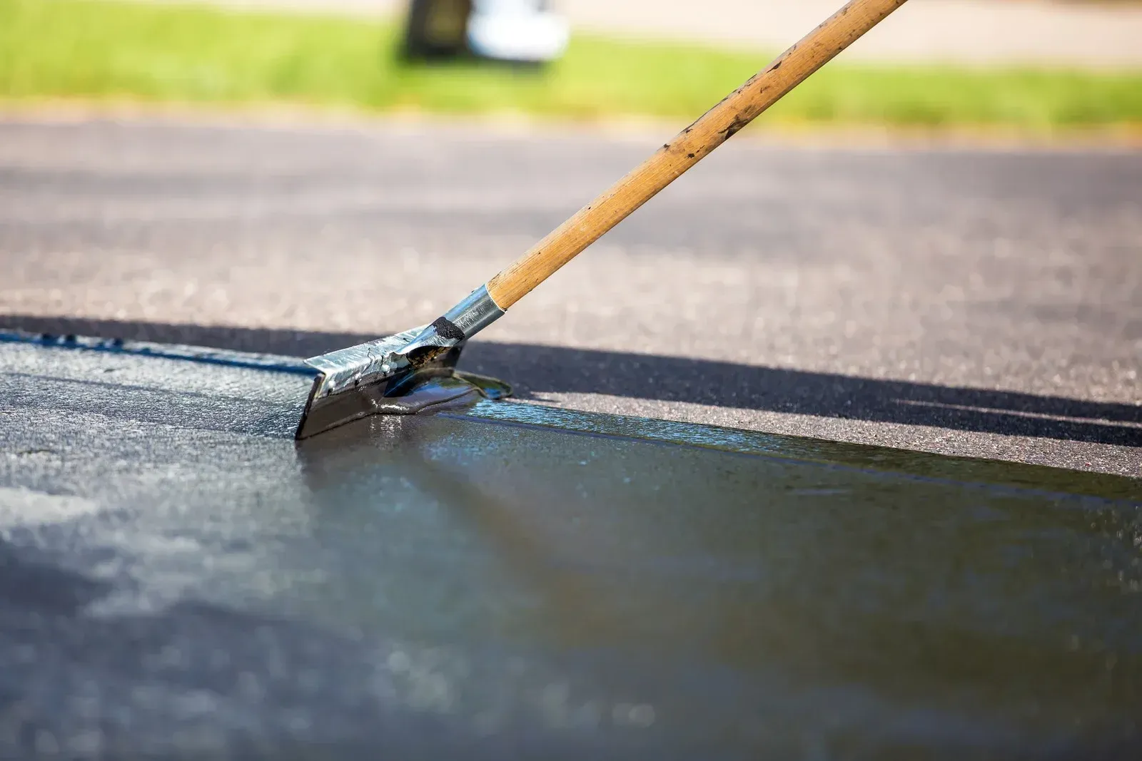 A person is using a rake to spread asphalt on a road.