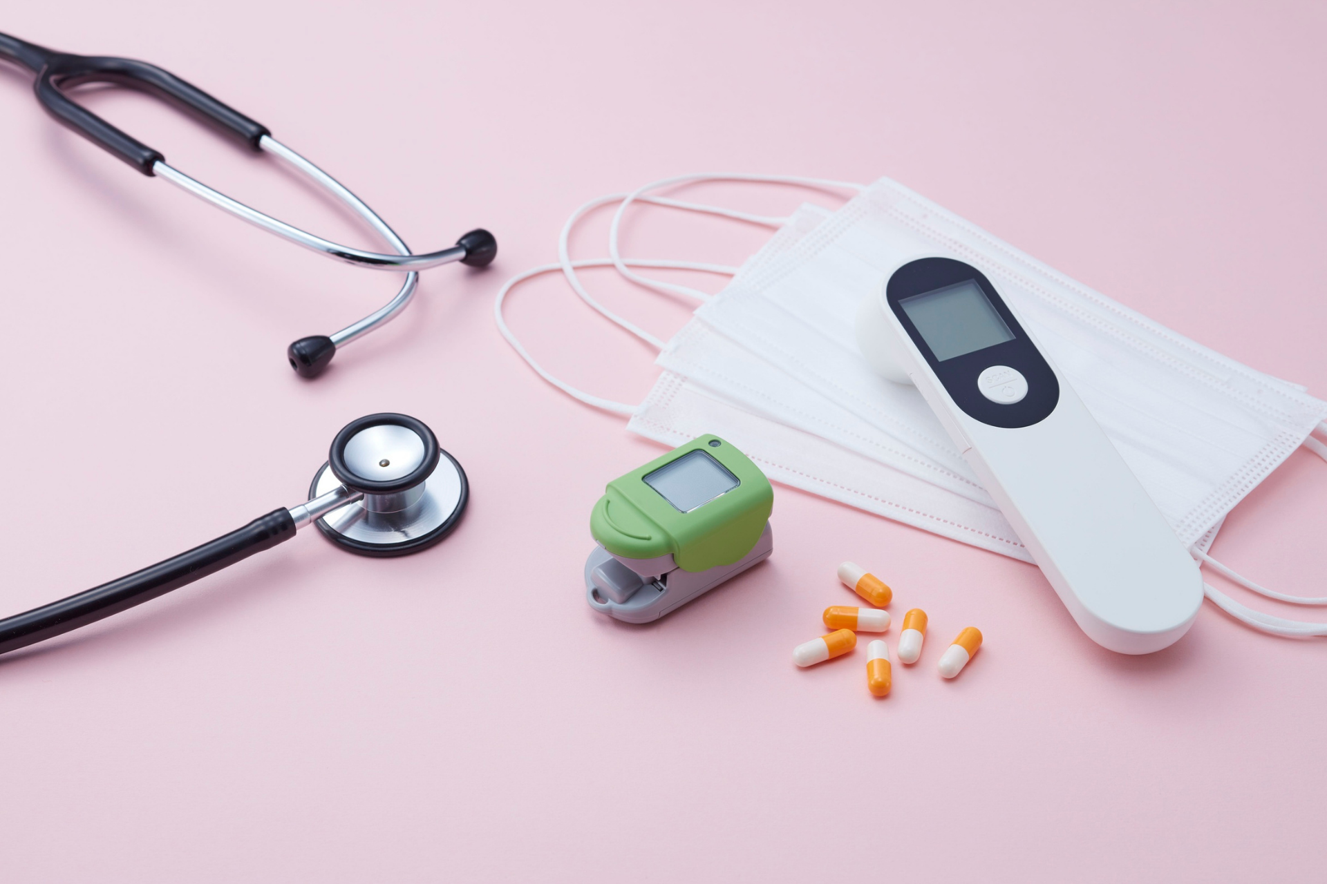 Medical supplies on a pink surface: stethoscopes, face masks, inhaler, and pills