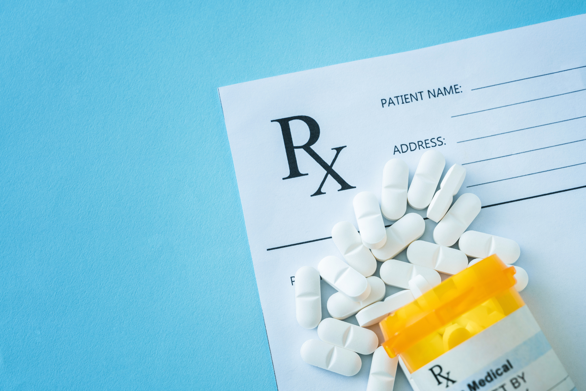 Prescription form with spilled white pills beside a yellow pill bottle on a blue background