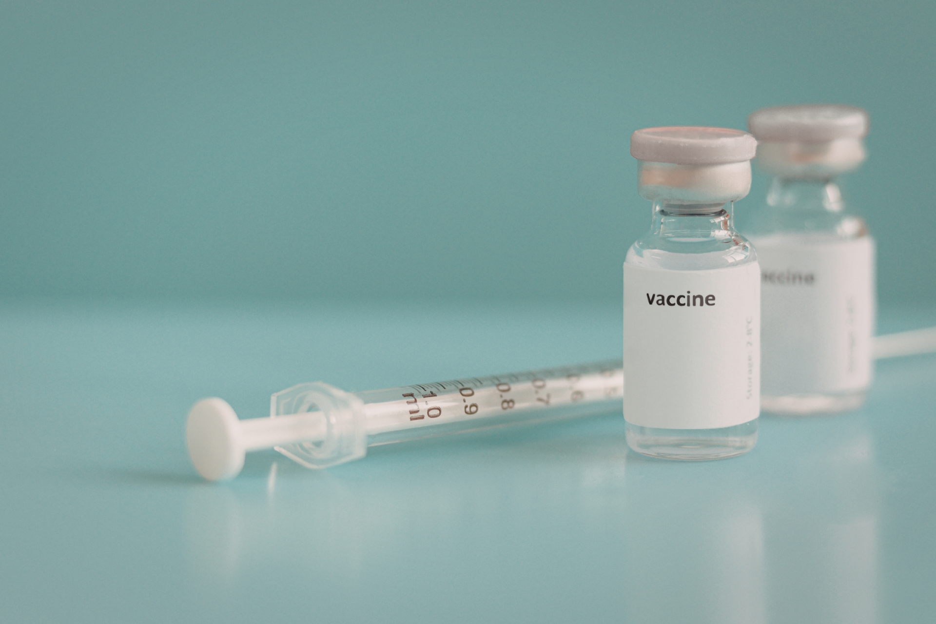 Vaccine vials and syringe on a blue surface with a teal background