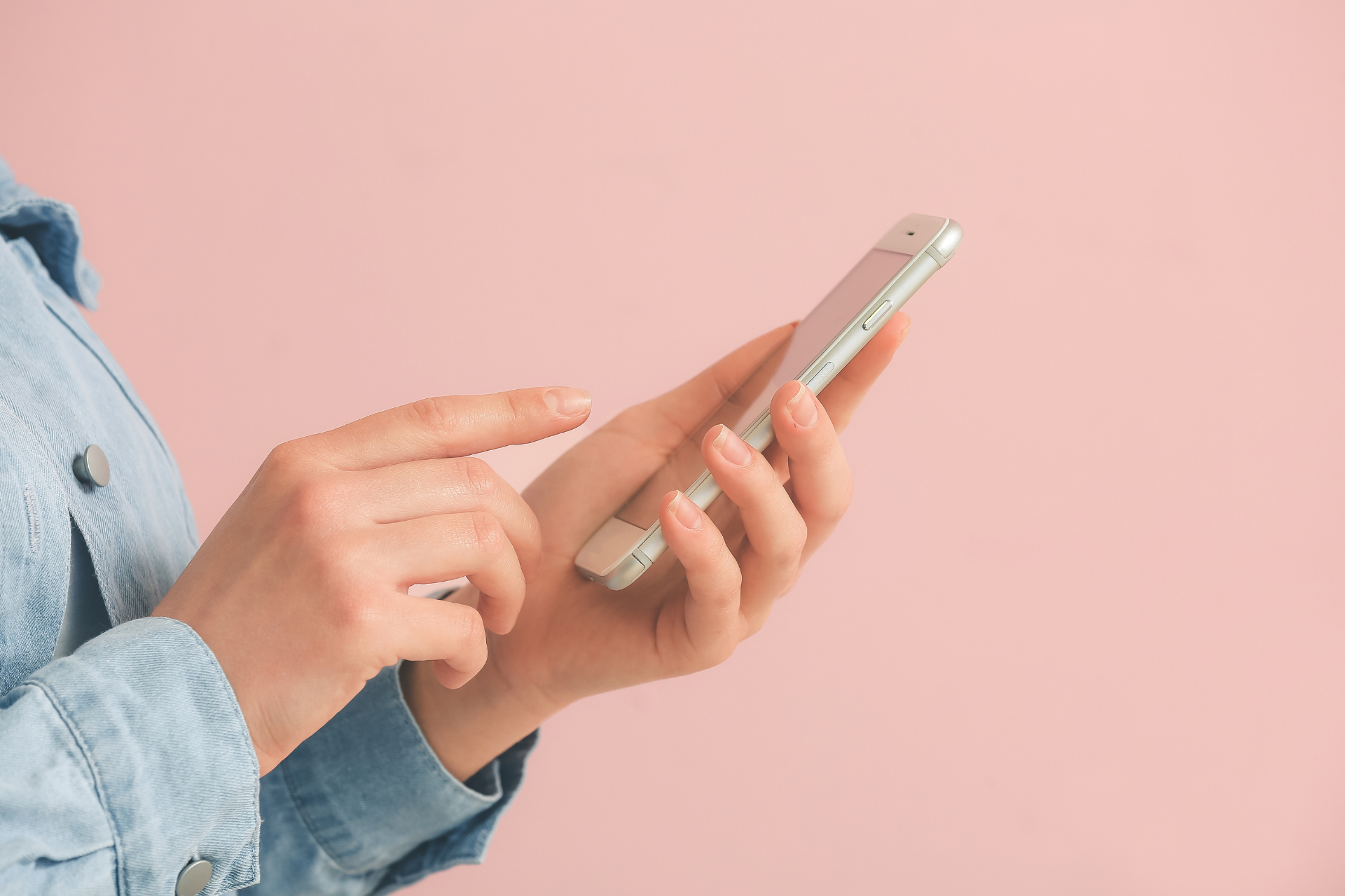 Hands using a smartphone against a pink background