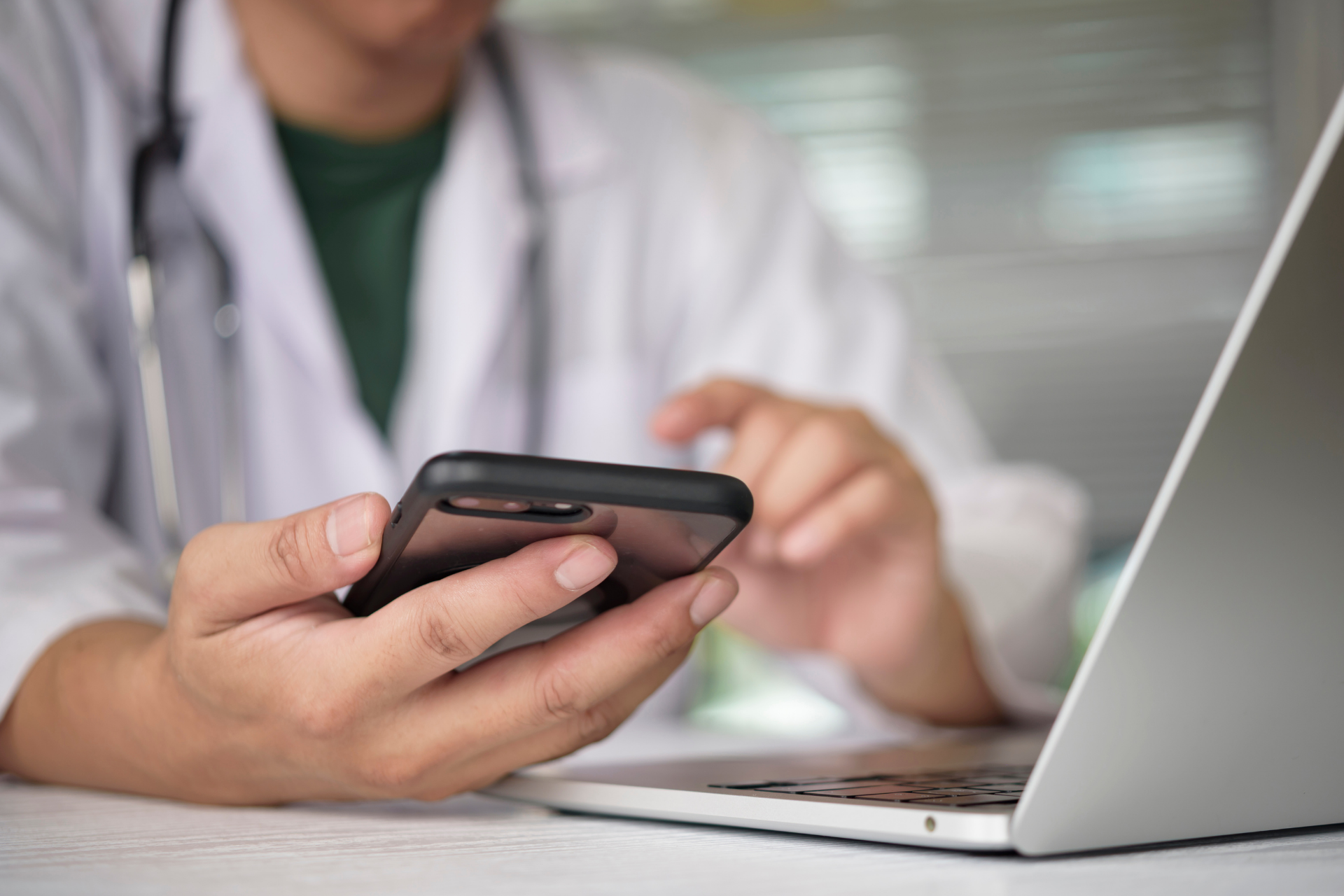 Doctor using a smartphone beside a laptop in a clinic office