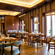 Warm, rustic restaurant dining room with wooden tables, chairs, brick walls, and pendant lights by tall windows