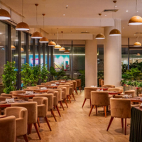 Empty modern restaurant dining room with tan chairs, wooden tables, and warm pendant lighting