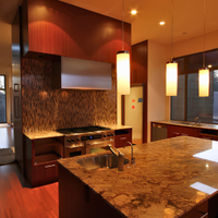 Modern kitchen with granite island, warm wood cabinetry, and large windows at sunset
