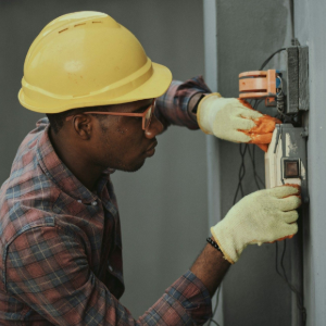 Worker in yellow hard hat adjusting an electrical panel on a wall