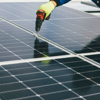 Worker cleaning solar panels with a squeegee, wearing gloves on a rooftop solar array
