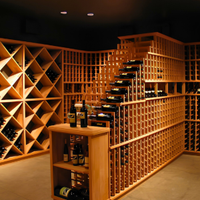 Warmly lit wine cellar with wooden racks, a central staircase, and bottles displayed on a small table.