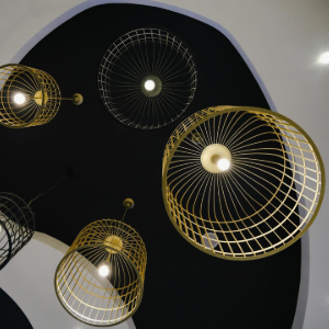 Abstract ceiling lights in gold, white, and black hanging against a black-and-white ceiling cutout.