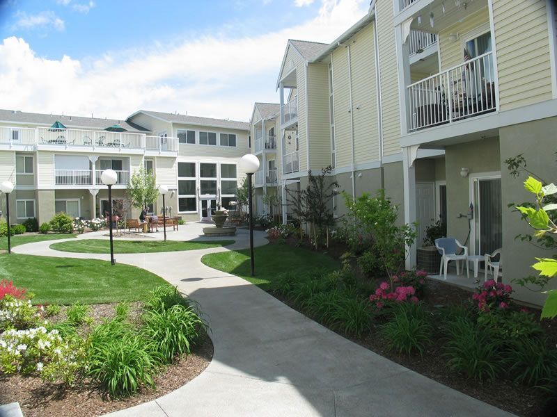 Apartment courtyard with winding walkway, landscaped gardens, and balconies under a clear blue sky