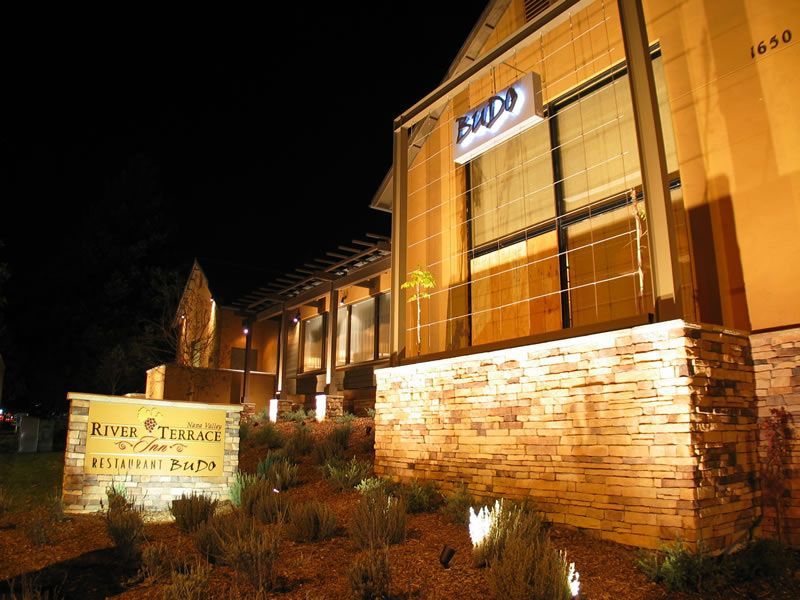 Night view of a lit brick building with a sign reading “River Terrace Restaurant Patio.”