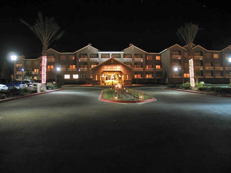Night-lit hotel entrance with a circular driveway and illuminated palm trees