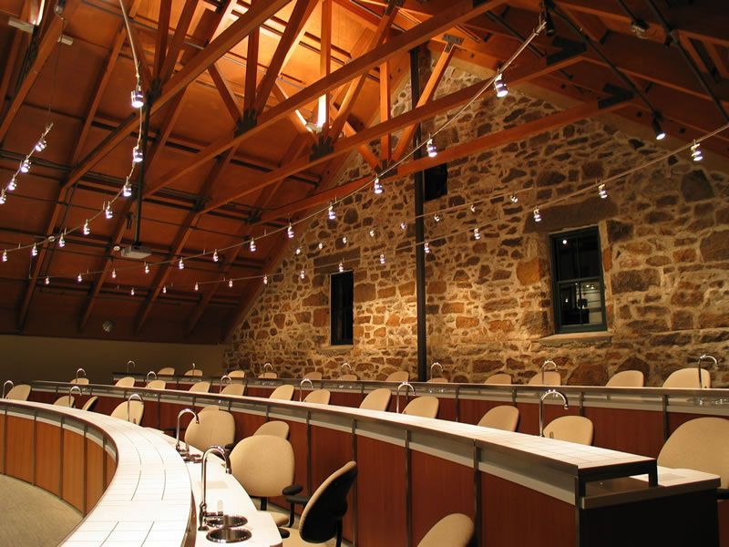 Curved auditorium with stone walls, wooden beams, and rows of beige seats under warm lighting