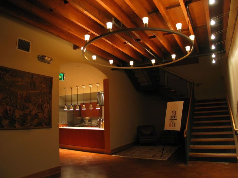 Warm-lit hotel lobby with wooden ceiling, staircase, reception desk, and circular chandelier.