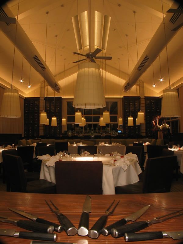 Elegant restaurant dining room with set tables, dark chairs, warm lighting, and modern ceiling fixtures