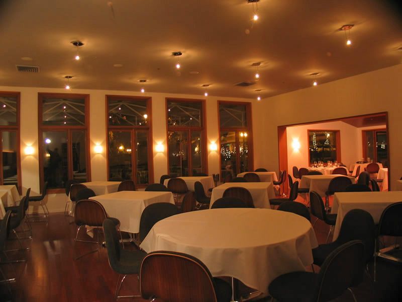 Dimly lit restaurant dining room with round tables, chairs, and warm overhead lights