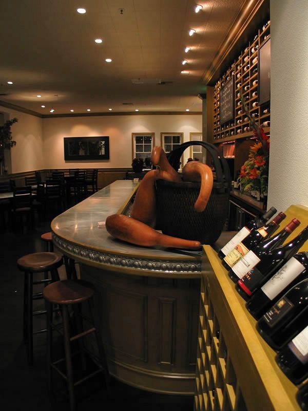 Cozy wine bar with a seated person at the counter, bottles on display, and warm ambient lighting