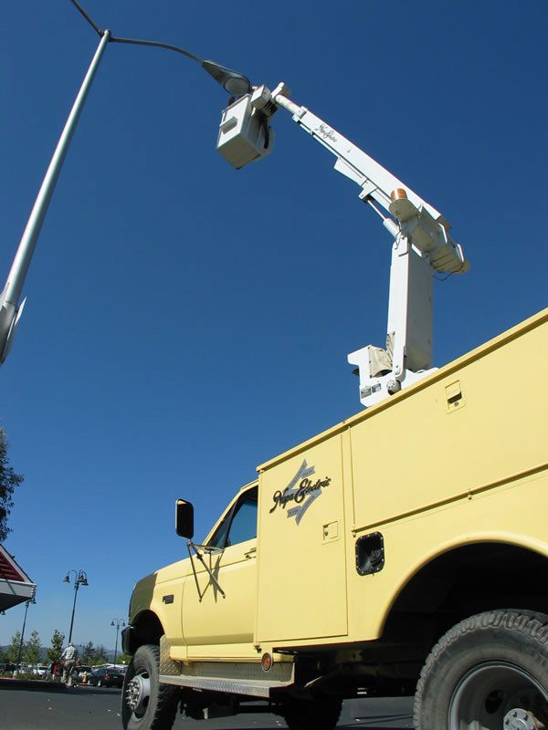 Yellow utility truck with raised bucket lift beside a streetlight against a blue sky