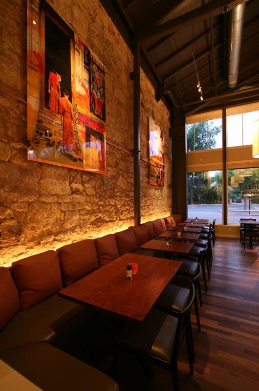 Cozy restaurant interior with stone walls, warm lighting, wooden tables, and chairs by large windows
