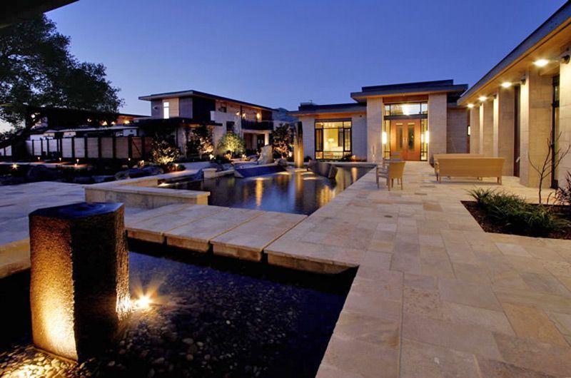 Luxury resort courtyard with pools, stone walkways, and warm evening lighting under a blue sky
