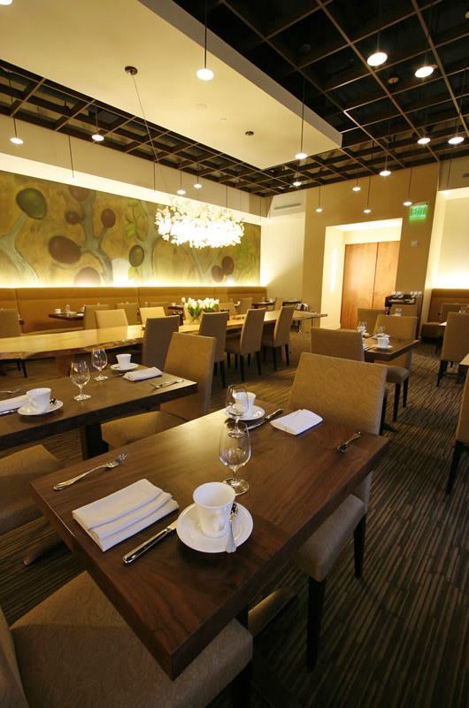 Warmly lit empty restaurant dining room with set wooden tables, beige chairs, and chandeliers